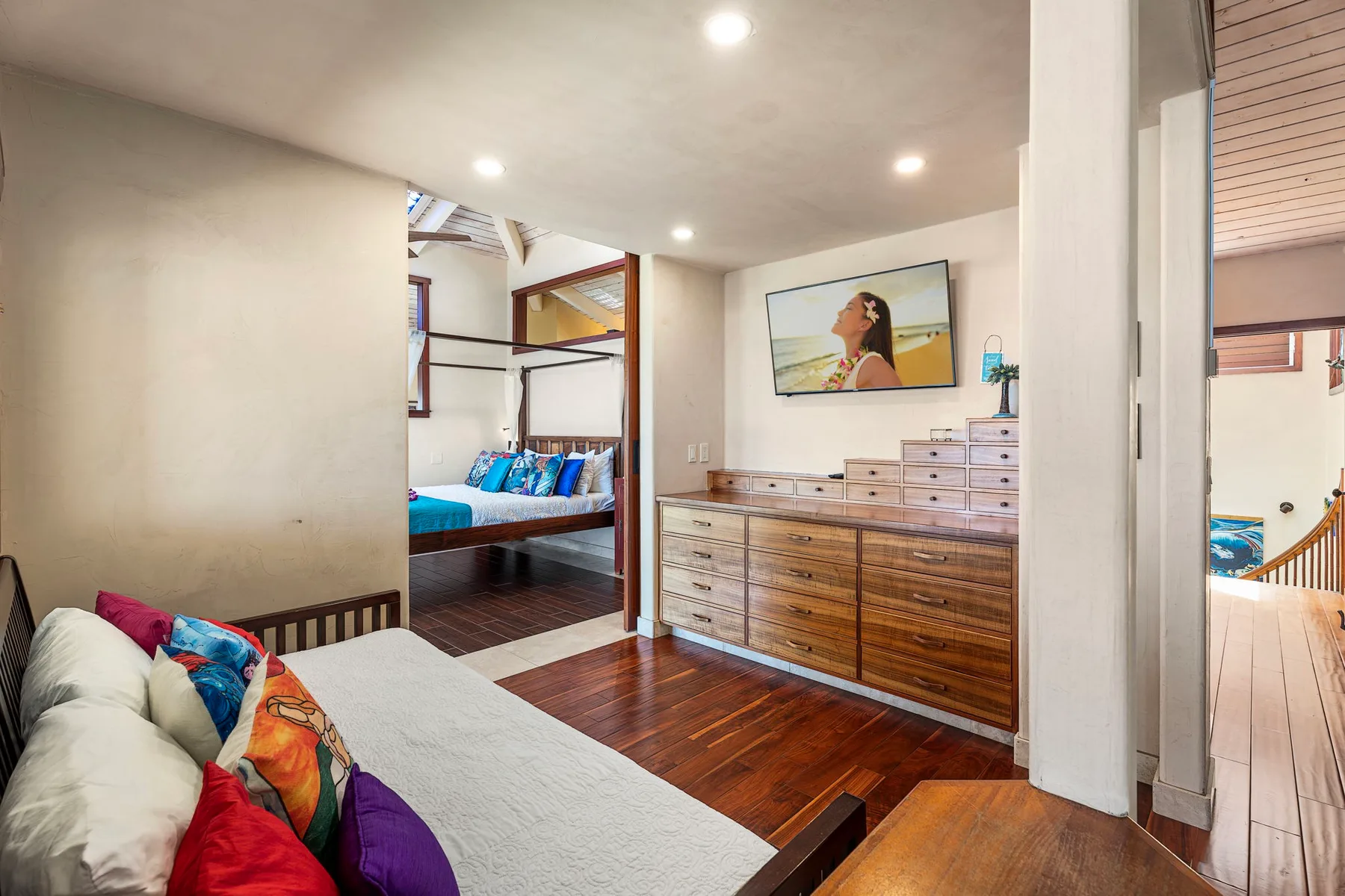 A bedroom with a bed, wooden dresser, and colorful cushions.