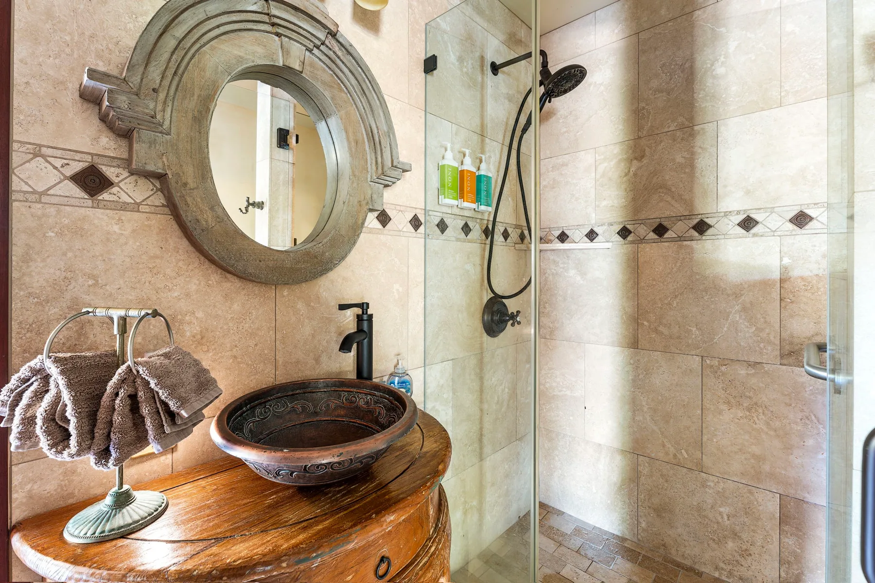 A tiled bathroom with a glass shower and a vessel sink on a wooden vanity.