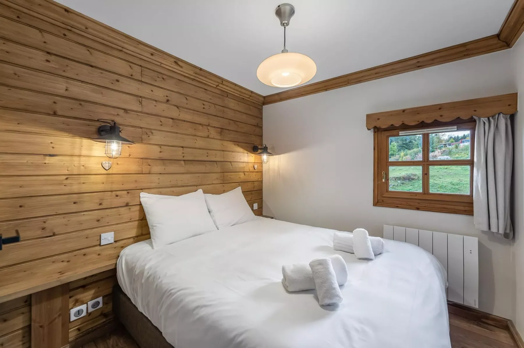 Un dormitorio con una cama blanca, paredes revestidas de madera y una ventana.