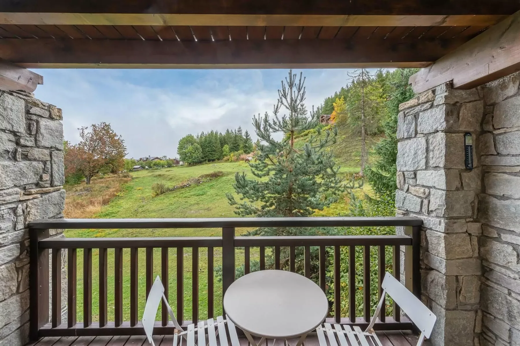 A covered balcony overlooks a grassy landscape with trees.