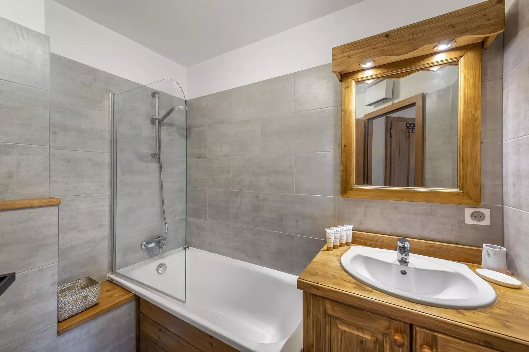 Un baño alicatado con bañera, mampara de ducha de vidrio y tocador de madera.