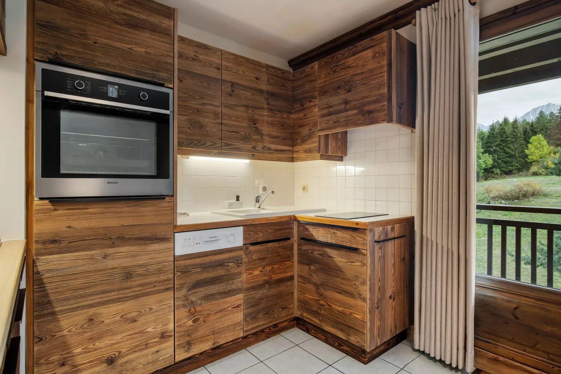 A wood-paneled kitchen with built-in appliances and a counter beside a curtained window.