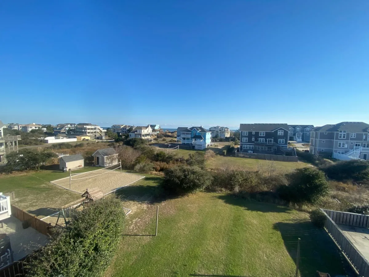 Un patio con césped, una pequeña cancha cercada y casas a lo lejos.