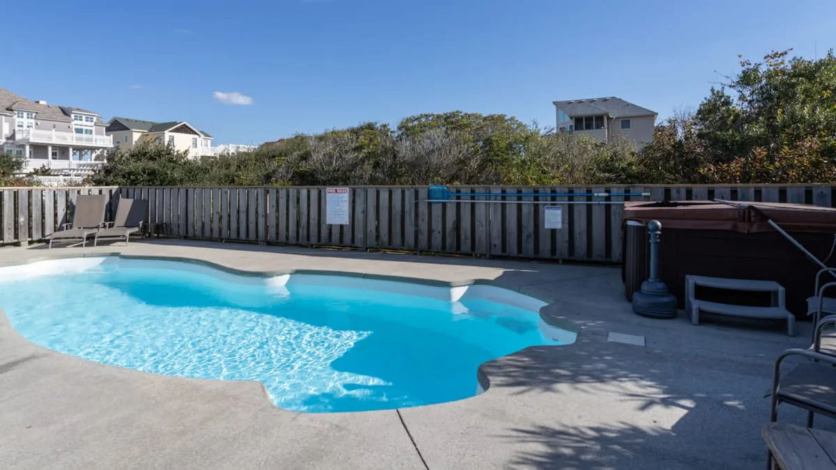 Una piscina al aire libre está junto a un patio cercado bajo un cielo despejado.