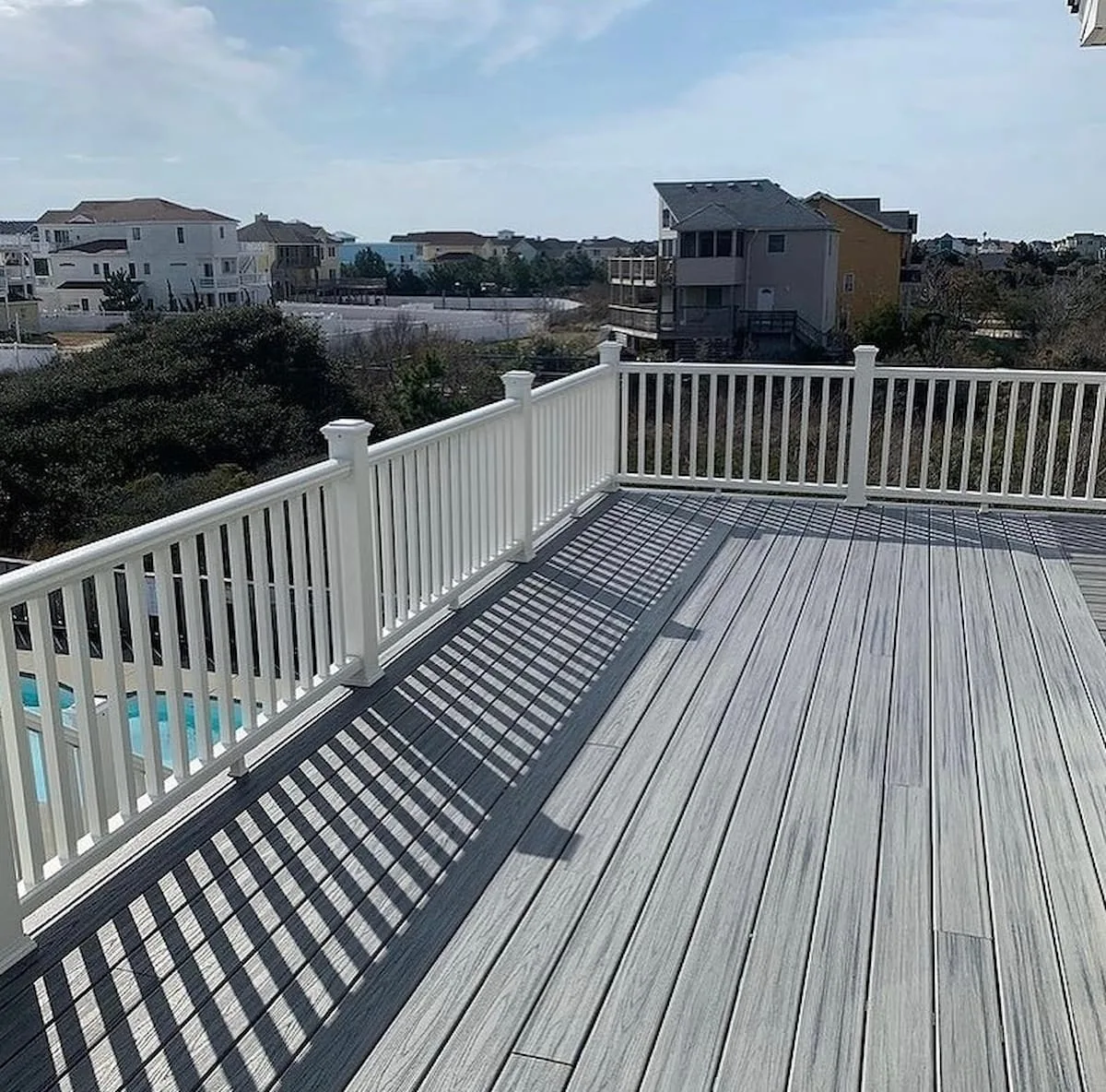 Una terraza elevada con barandillas blancas da a casas y vegetación cercanas.