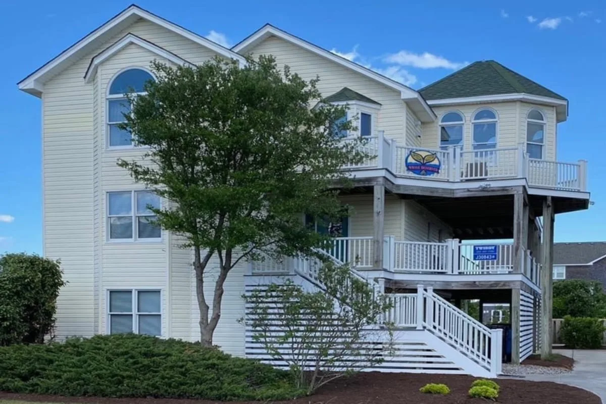 Una casa grande de color claro con una terraza elevada y escaleras exteriores.