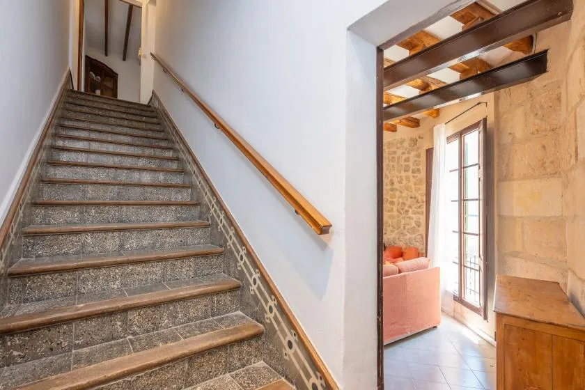 Una escalera de piedra sube junto a una puerta abierta hacia una luminosa zona de estar.