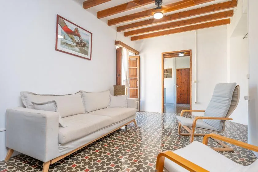 Una sala luminosa tiene asientos claros, suelo de baldosas estampadas y vigas de madera a la vista.