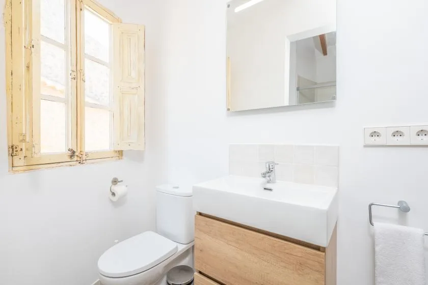 Un baño luminoso con lavabo, inodoro y una ventana de madera abierta.