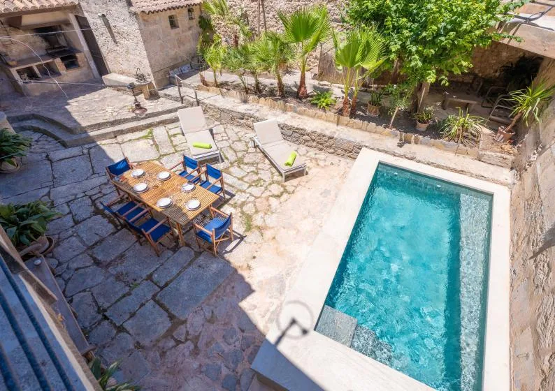 Un patio de piedra con piscina, mesa de comedor al aire libre y vegetación alrededor.