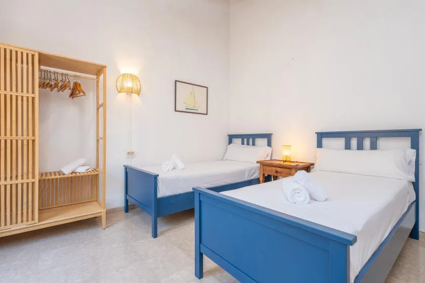 Un dormitorio con dos camas azules, ropa de cama blanca y un armario de madera.
