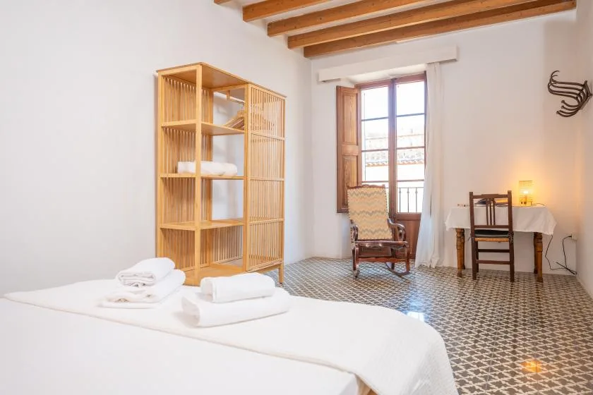 Un dormitorio con una cama, estantería abierta y una mesa junto a la ventana.