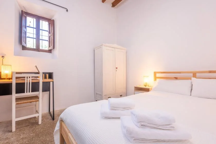 Un dormitorio con una cama grande, toallas dobladas y un escritorio pequeño bajo la ventana.