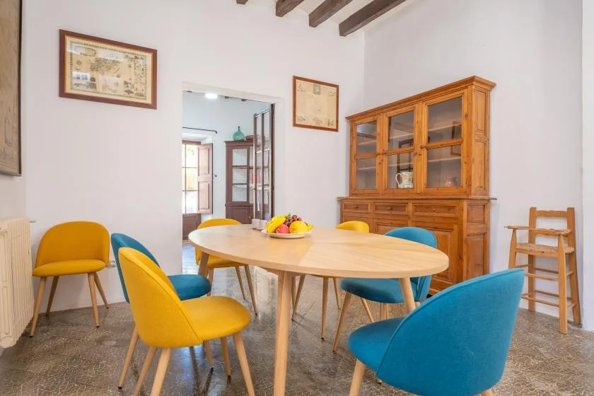 Comedor con una mesa redonda, sillas de colores y un mueble de madera.