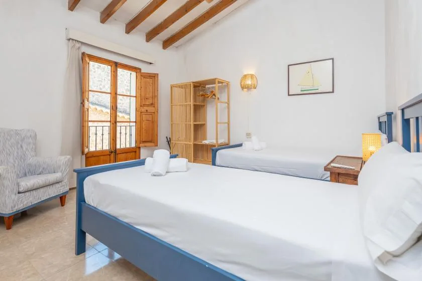 Un dormitorio con ropa de cama blanca, camas con estructura azul y vigas de madera a la vista.