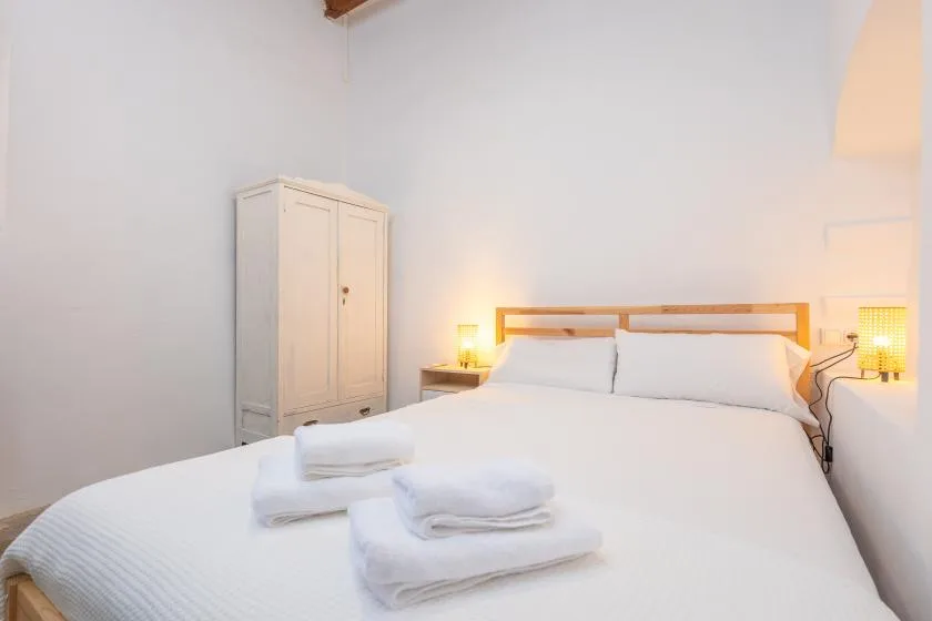 Un dormitorio con una cama blanca, toallas dobladas y un armario.