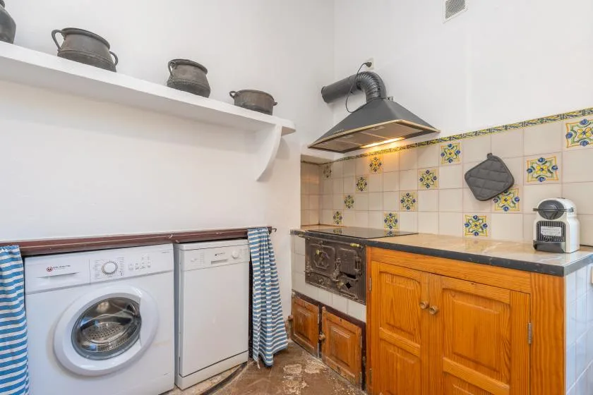 Una cocina compacta con lavadora, azulejos decorativos y gabinetes de madera.