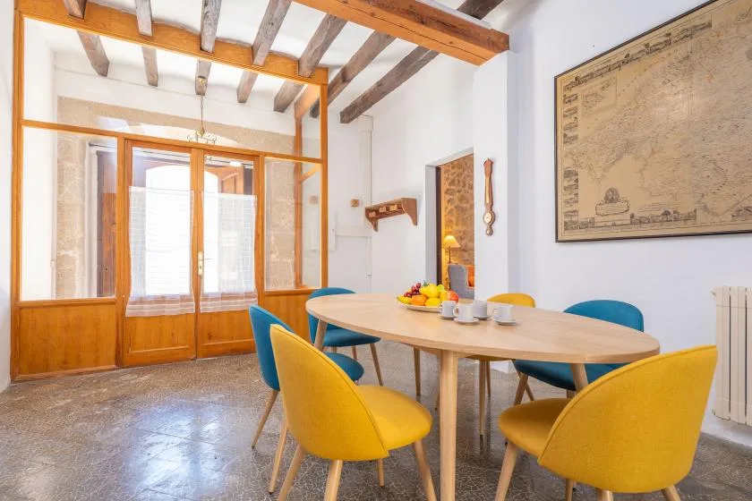 Comedor con una mesa, asientos de colores y vigas a la vista en el techo.