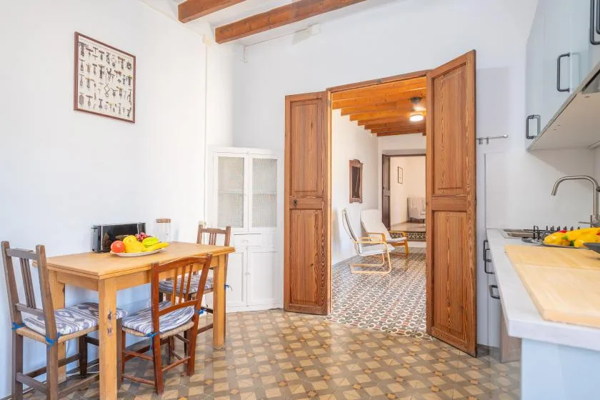 Un comedor con mesa y sillas de madera se abre a una habitación contigua con suelo de baldosas.