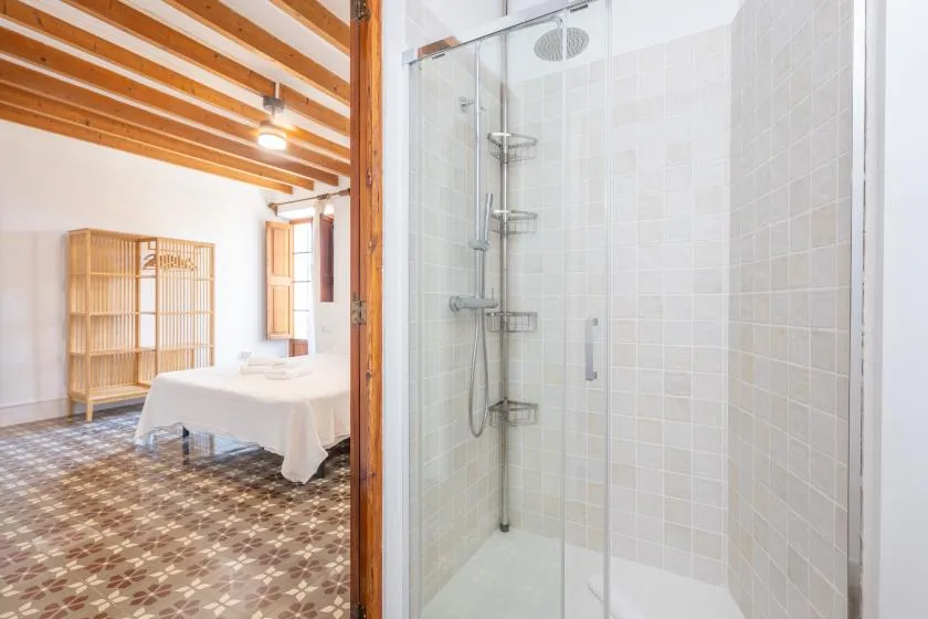 Una zona de ducha con azulejos junto a un dormitorio con cama y vigas de madera a la vista.