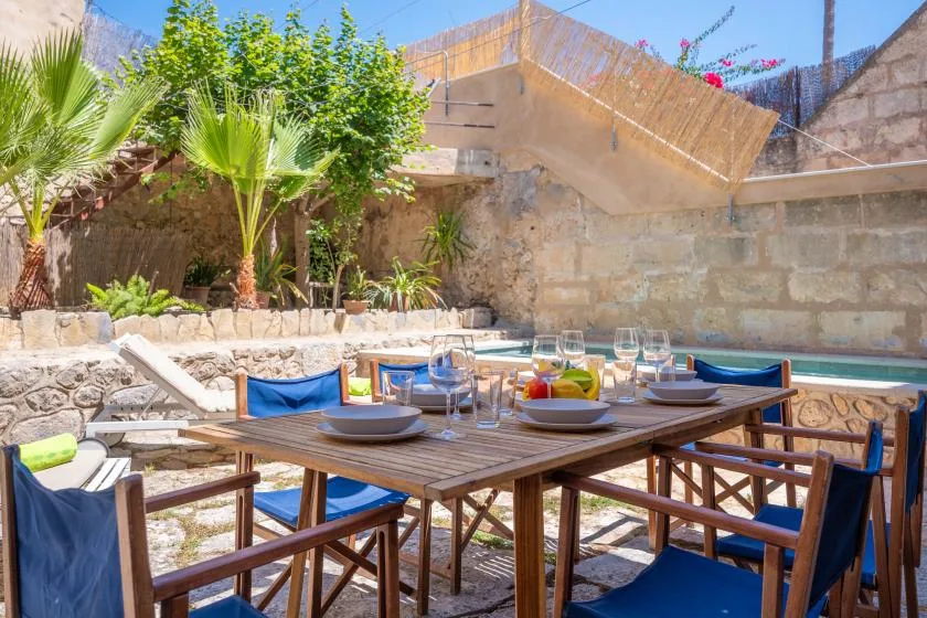 Un comedor al aire libre con una mesa de madera junto a una piscina.