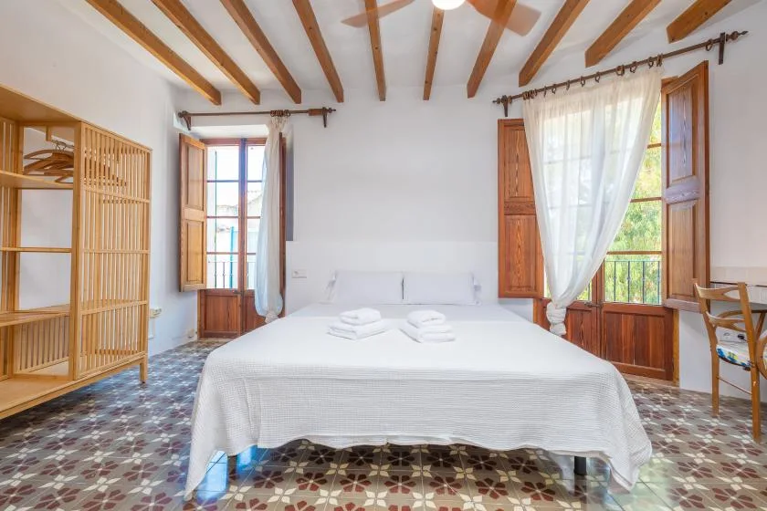 Un dormitorio luminoso con una cama blanca y contraventanas de madera abiertas.