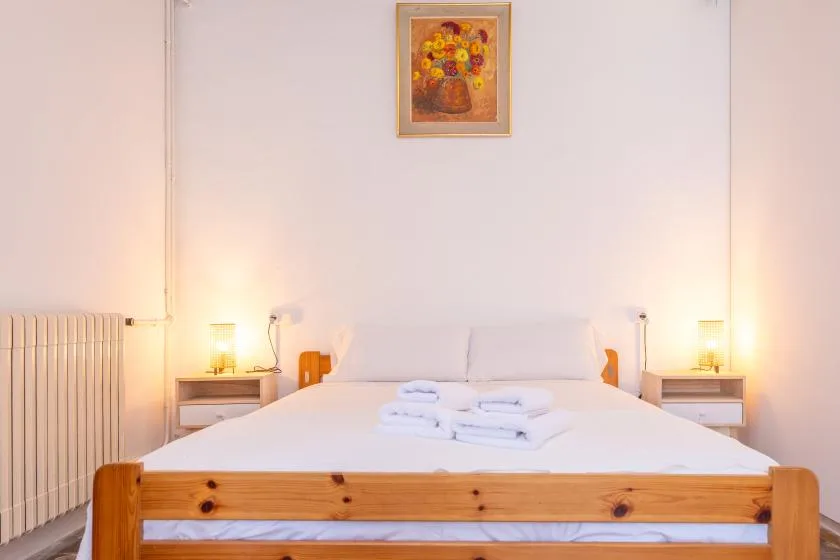 Un dormitorio con una cama de madera, toallas dobladas y un cuadro floral enmarcado.