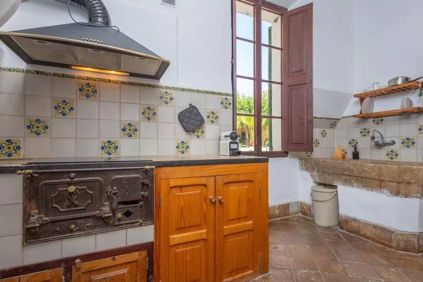 Una cocina alicatada con cocina, armarios de madera y una ventana abierta.