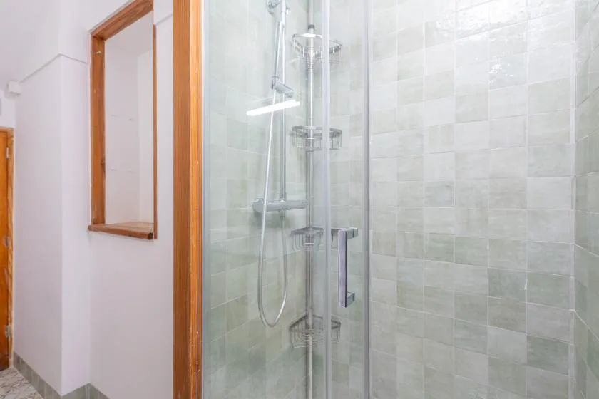 Baño con azulejos, ducha de vidrio y molduras de madera.