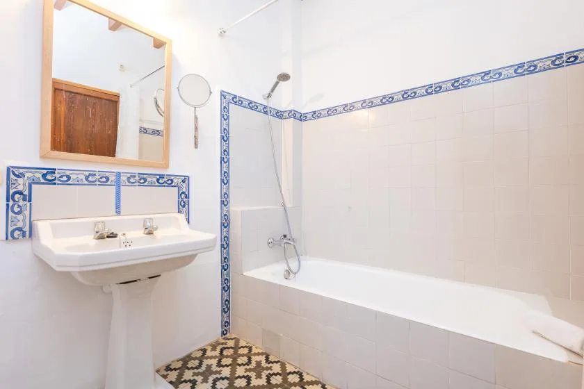 Un baño alicatado cuenta con bañera, ducha y lavabo de pared.