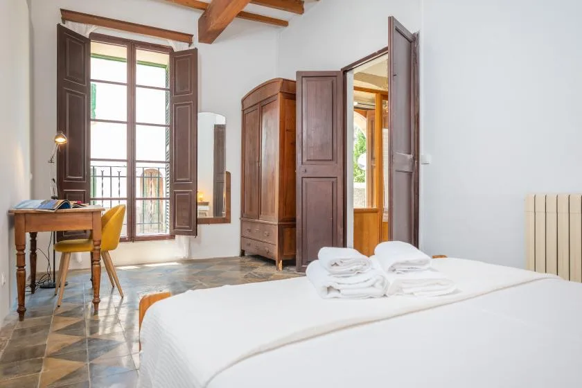 Un dormitorio luminoso con cama, armario de madera y escritorio junto a una ventana alta.