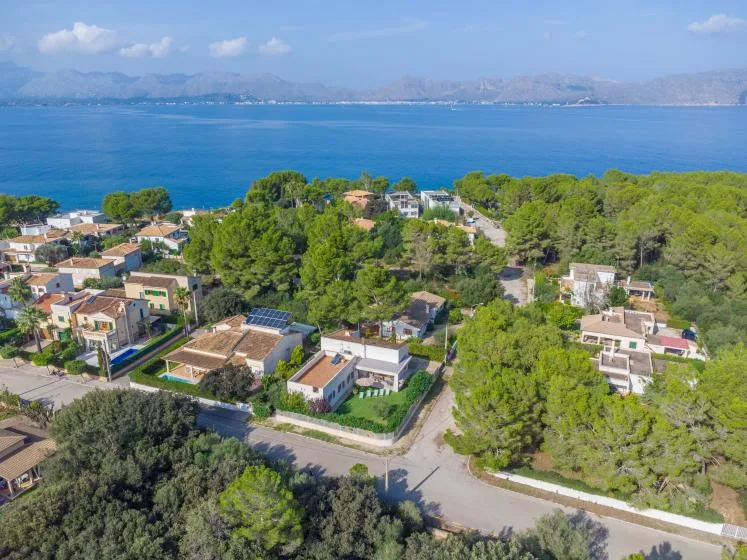 Vista aérea de una zona residencial costera con el mar y montañas a lo lejos.