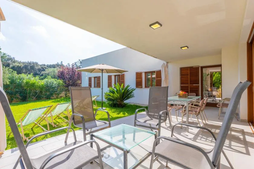 Un patio cubierto con asientos al aire libre y una mesa de vidrio da a un jardín.
