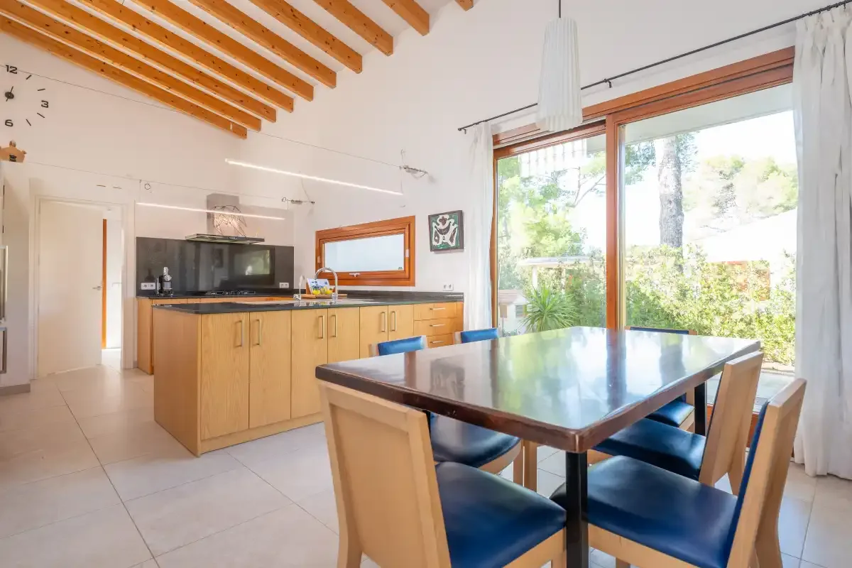 Cocina y comedor con gabinetes de madera y una mesa junto a grandes ventanales.
