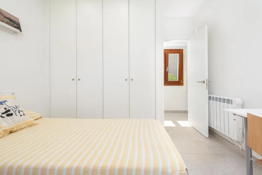 Un dormitorio luminoso con una cama, armarios empotrados y una puerta abierta.