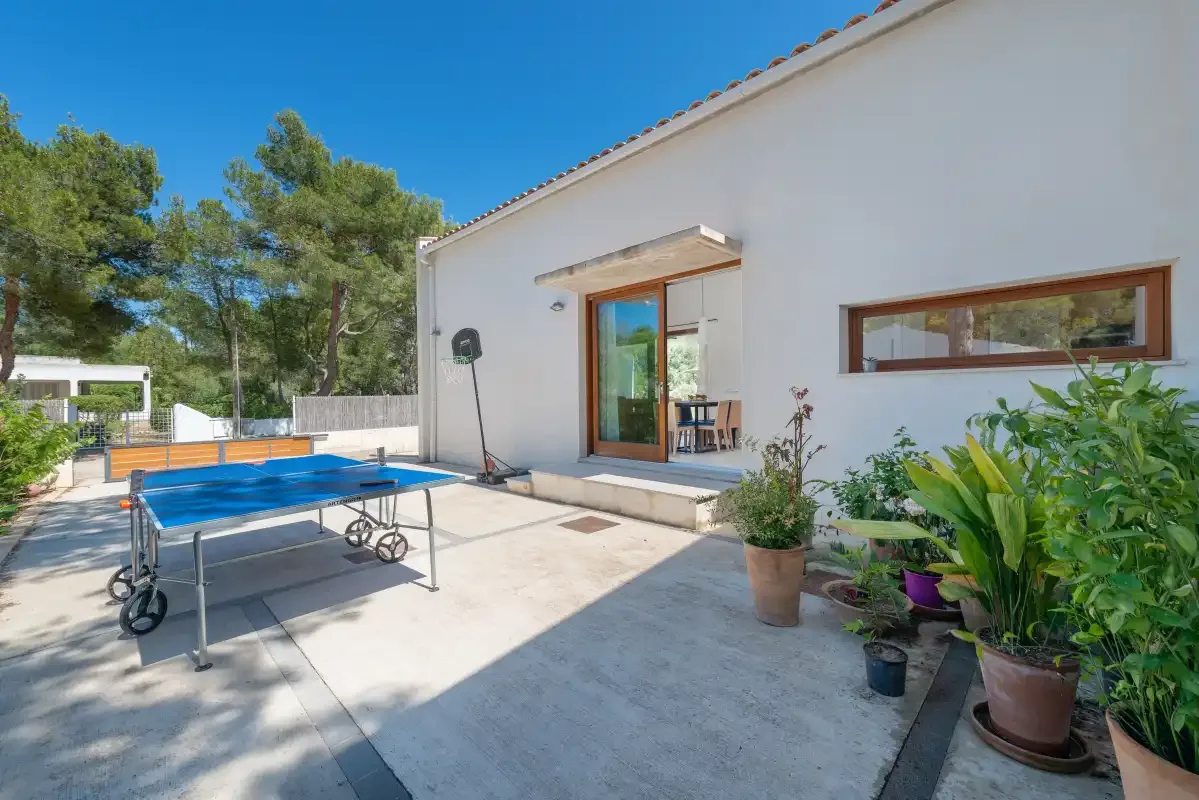 Un patio soleado con una mesa de ping-pong azul junto a una casa blanca.
