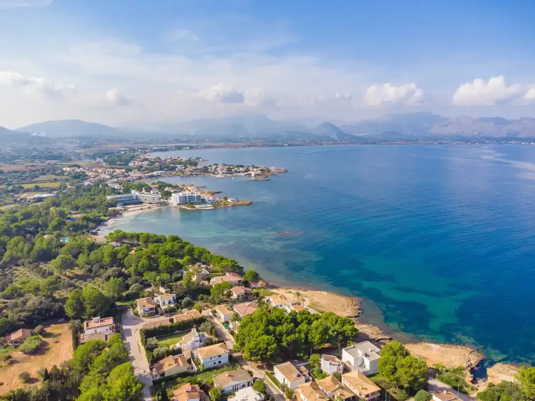 Una vista aérea de la costa muestra una bahía curva, vegetación y montañas lejanas.