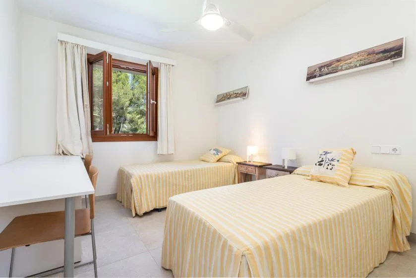Un dormitorio luminoso con dos camas individuales y una ventana con vistas a la vegetación.
