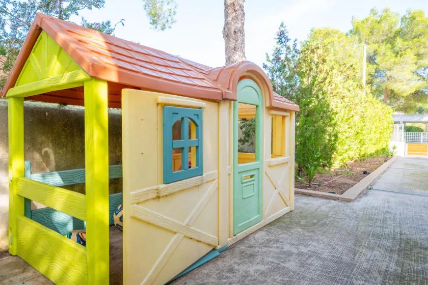 Una colorida casita de juegos al aire libre está junto a un camino pavimentado.