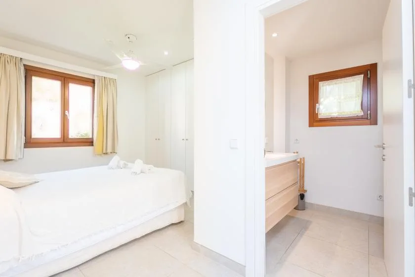 Un dormitorio luminoso con una cama blanca y un baño contiguo.