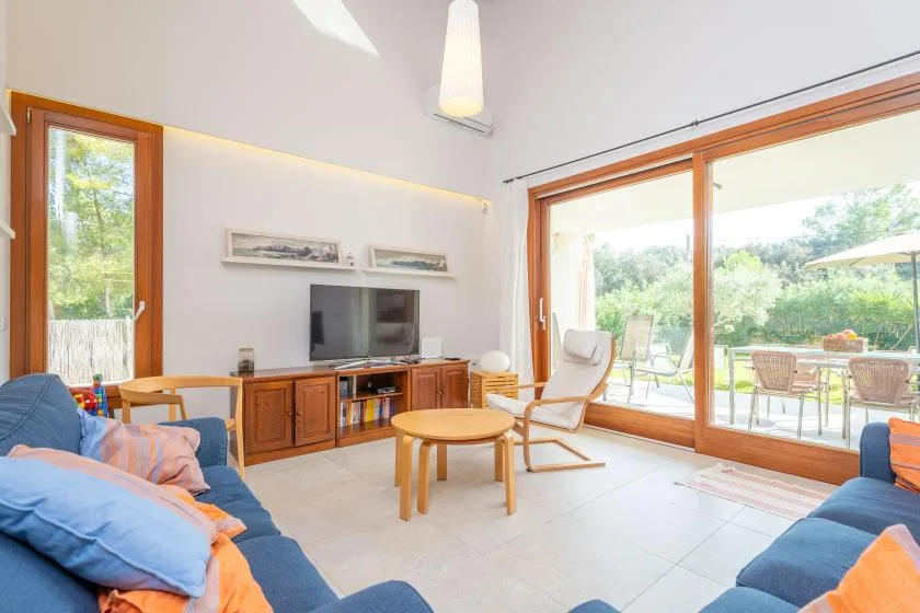 Una sala luminosa con asientos, un televisor y grandes puertas de vidrio que dan a un patio.