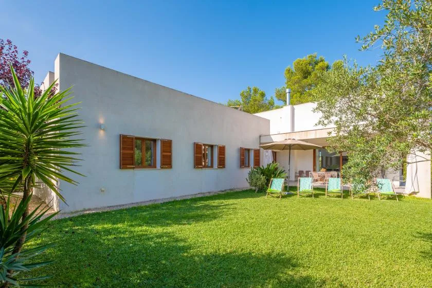 Una casa moderna da a un césped verde con asientos al aire libre bajo un toldo.