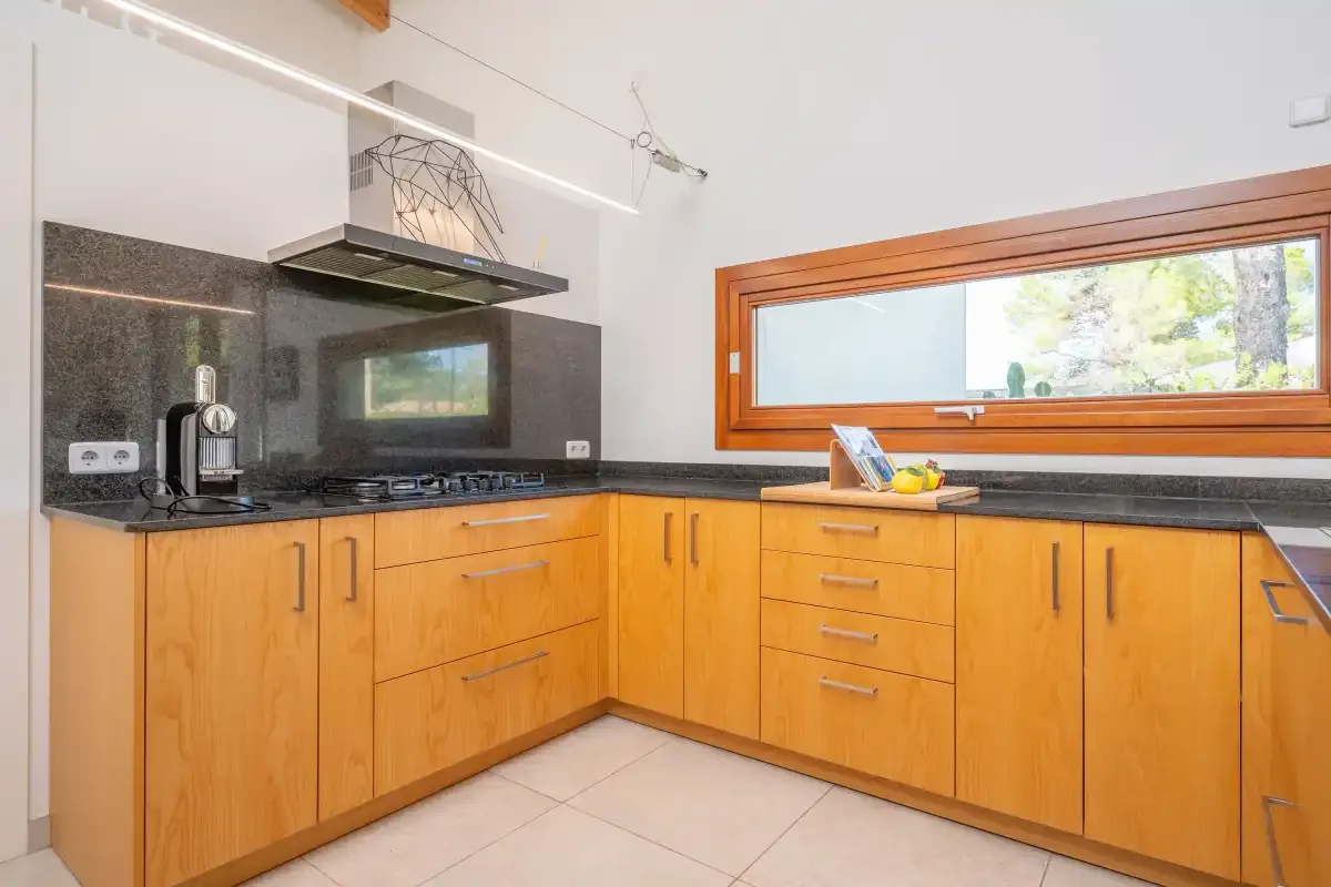 Una cocina luminosa con gabinetes de madera, encimeras oscuras y una ventana horizontal amplia.
