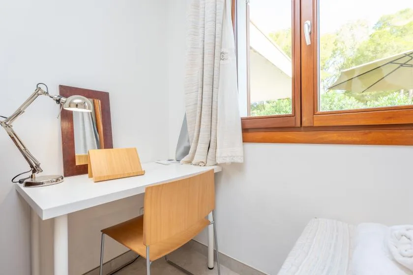 Un espacio de trabajo en el dormitorio está junto a una ventana, con escritorio y silla.