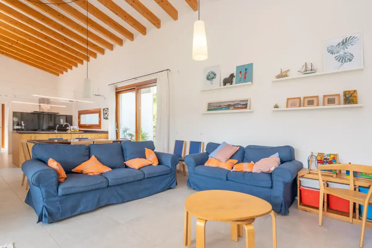 Sala de estar con asientos azules, una mesa de centro redonda y vigas de madera a la vista.