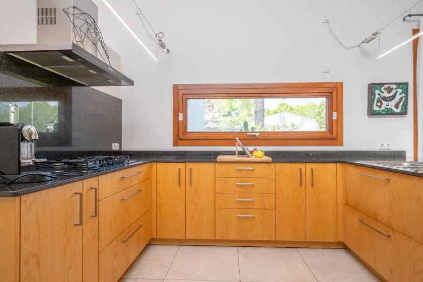 Una cocina con gabinetes de madera, encimeras oscuras y una ventana amplia.