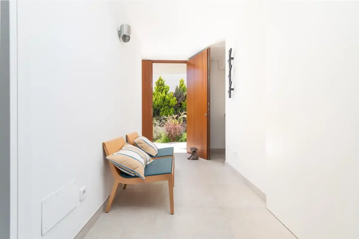 Un pasillo luminoso con una puerta de madera abierta al jardín y una pequeña zona de estar.