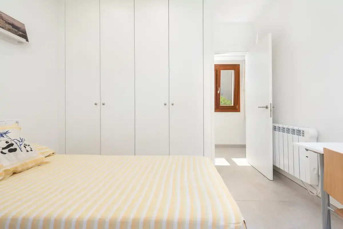 Un dormitorio luminoso con una cama, armarios empotrados y una puerta abierta.