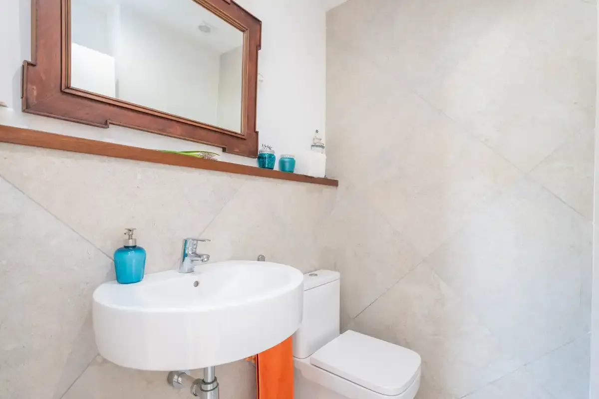 Un baño con lavabo suspendido, espejo e inodoro.