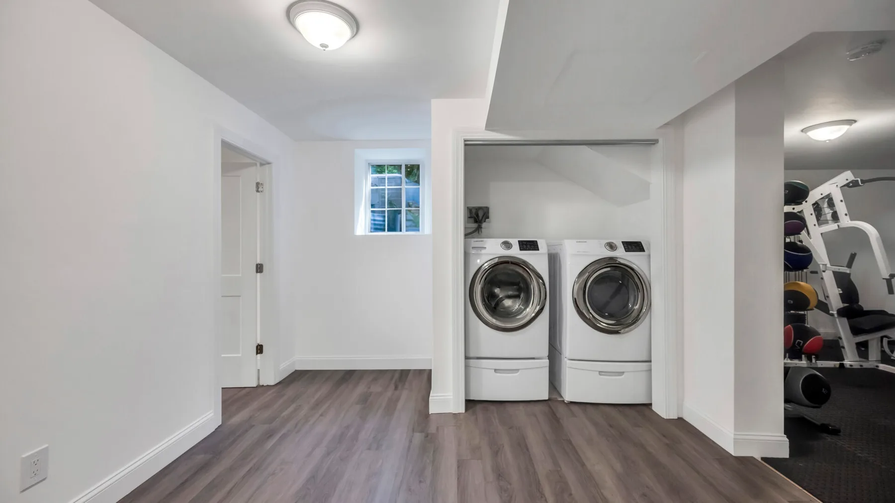 A laundry room with two front-loading machines beside an open exercise area.